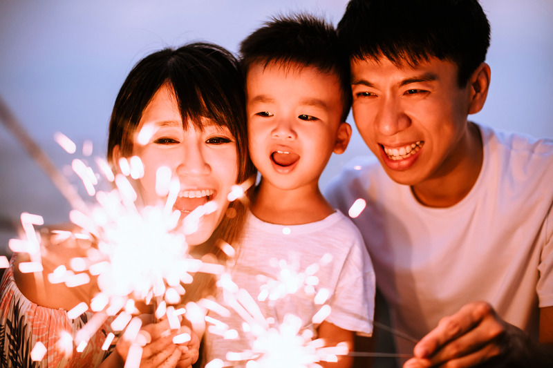 Two parents and a child play with sparklers on the 4th of July.