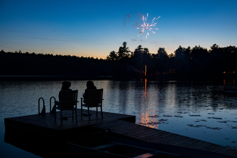 Fireworks seen at a distance from a private dock on a lake. 